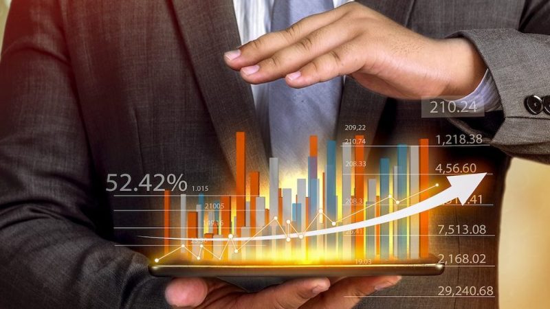 Business people hold a tablet, plan and strategy and display virtual holograms of statistics, financial graphs, securities and charts on a dark background. The concept of business growth
