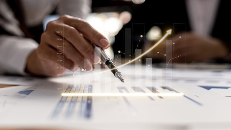 Two businessmen are meeting together, they point to financial documents to discuss plans and solutions, chart graphics showing financial status and performance. Business administration concept.
