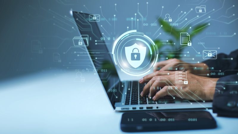 A businessman works on his laptop at home with a virtual display showing a symbol to signify cyber security privacy and online data protection.