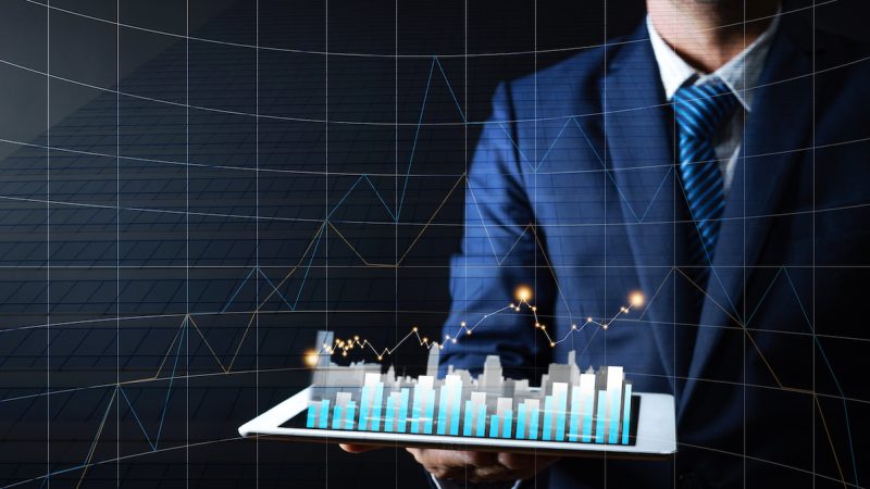 Business man holding tablet with graph and building on dark background, finance and residence stock market growing up concept