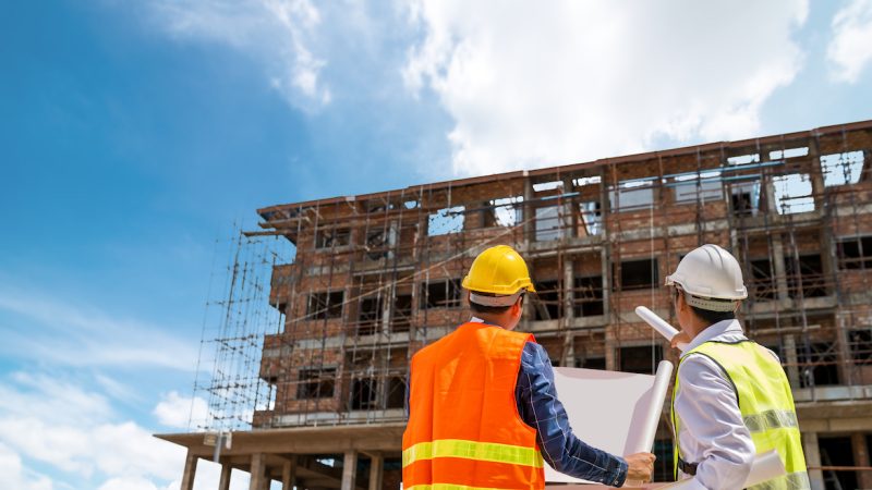 Businessman engineer looking blueprint in a building to  discussion with architects at construction site or building site of highrise building