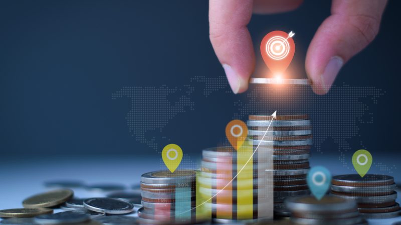 Set financial goals concept. Businessman is tapping on top of coins, setting business and financial goals, saving money, investing money, growing business graph, increasing profit on investment.