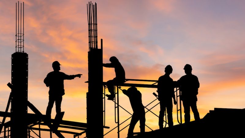 Silhouette of Engineer and worker on building site, construction site at sunset in evening time.