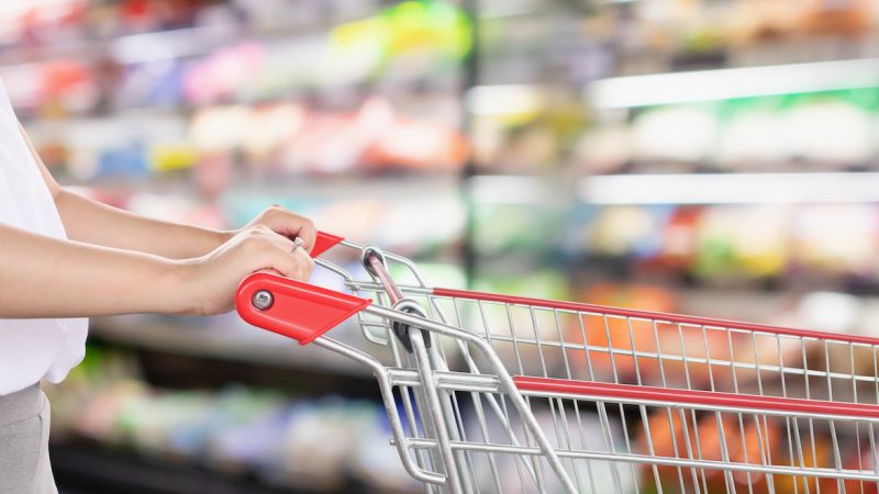Woman hold shopping cart with abstract blur supermarket discount store aisle and product shelves interior defocused bokeh background